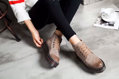 Person schnürt beigefarbene Schnürschuhe, daneben ein aufgeschlagenes Magazin