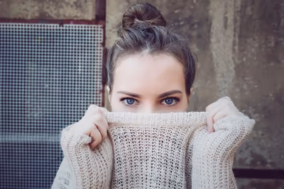 Junge Frau zieht den Kragen eines hellen Strickpullovers über das Gesicht