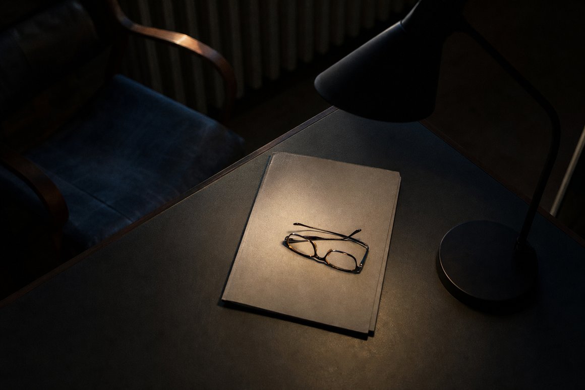 Geschlossener Ordner und zusammengelegte Lesebrille auf einem Schreibtisch im Lampenlicht